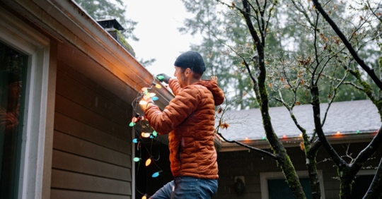 man putting up holiday lights on roof